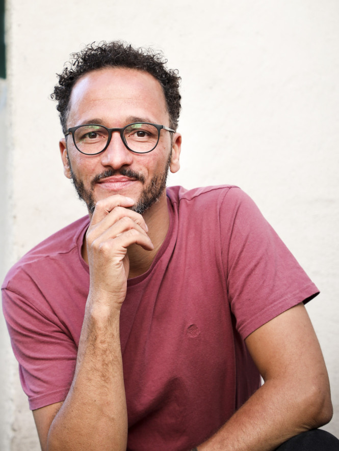 Lebensberater Franz Wilhelm blickt ruhig und freundlich. Er sitzt vor einem Haus und st&uuml;tzt seinen Kopf mit seiner Hand am Kinn.